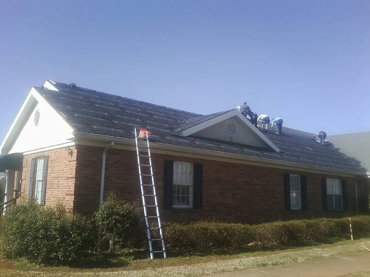 Crew tearing shingles off a brick ranch roof with a ladder set — Emergency Roof Repair work by our crew in Paradise