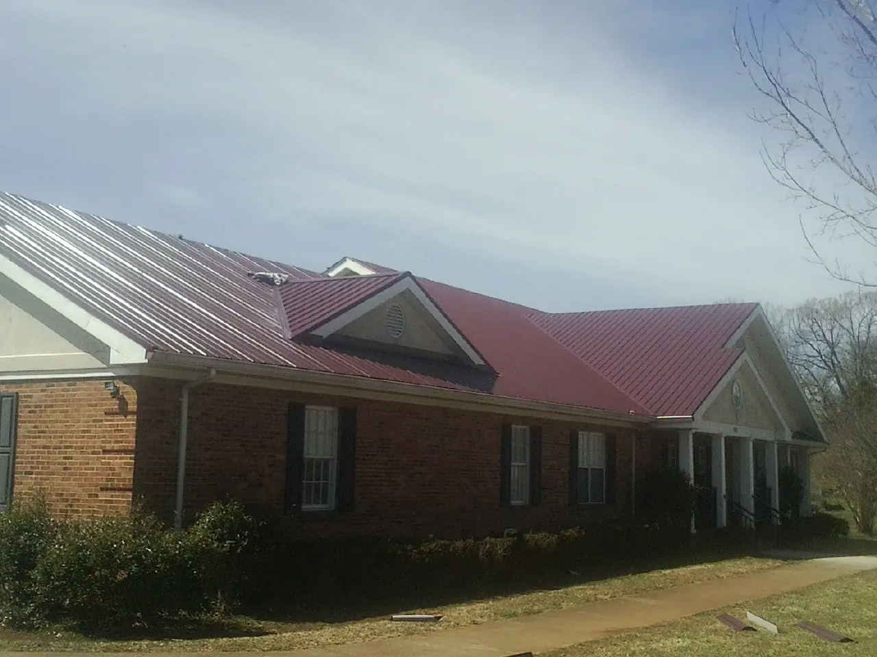 Red metal roof with gabled entries on a long brick building, from a Hail Damage Roof Repair job in Paradise